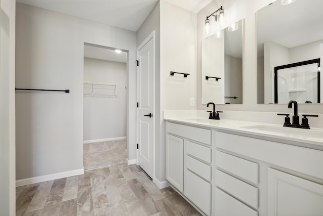 bathroom featuring baseboards, a spacious closet, double vanity, and a sink