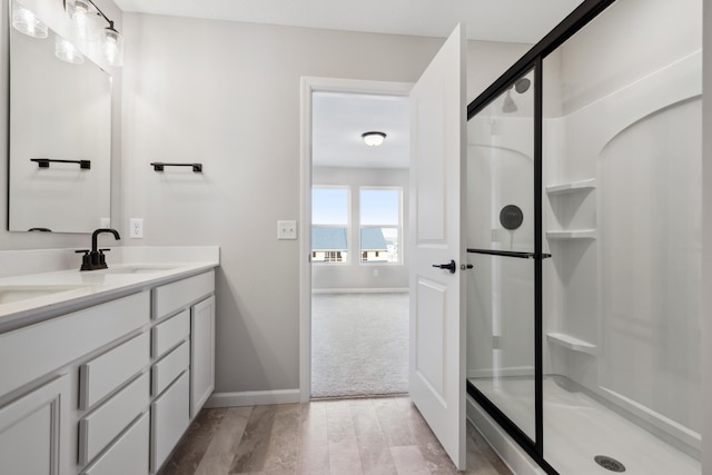 bathroom with baseboards, a stall shower, double vanity, and a sink