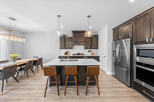 kitchen with a sink, stainless steel appliances, light wood-style flooring, backsplash, and dark brown cabinets