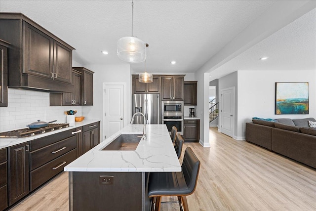 kitchen with light wood finished floors, a sink, decorative backsplash, appliances with stainless steel finishes, and open floor plan