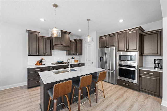 kitchen with a sink, appliances with stainless steel finishes, decorative backsplash, light wood-type flooring, and dark brown cabinets