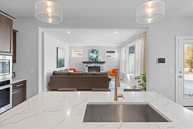 kitchen with a sink, dark brown cabinetry, decorative light fixtures, light stone counters, and appliances with stainless steel finishes