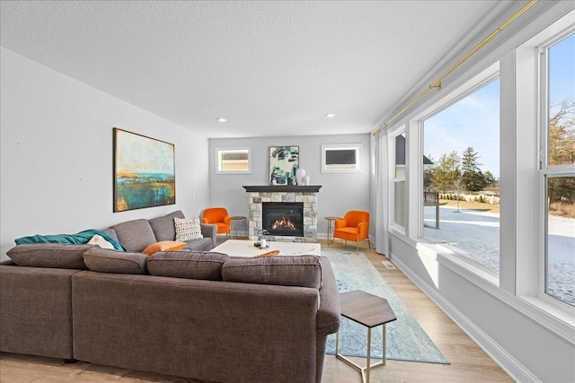 living room featuring recessed lighting, a stone fireplace, light wood finished floors, baseboards, and a textured ceiling