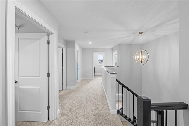 corridor with a chandelier, carpet, an upstairs landing, baseboards, and a textured ceiling