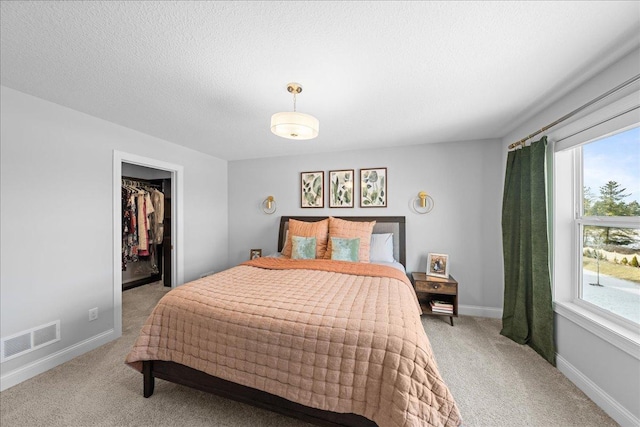 bedroom featuring visible vents, light carpet, baseboards, a textured ceiling, and a spacious closet