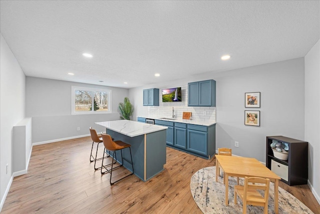 kitchen featuring light wood finished floors, decorative backsplash, blue cabinetry, a center island, and a breakfast bar area