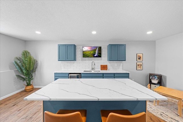 kitchen with a breakfast bar, a sink, light wood-style flooring, and blue cabinetry