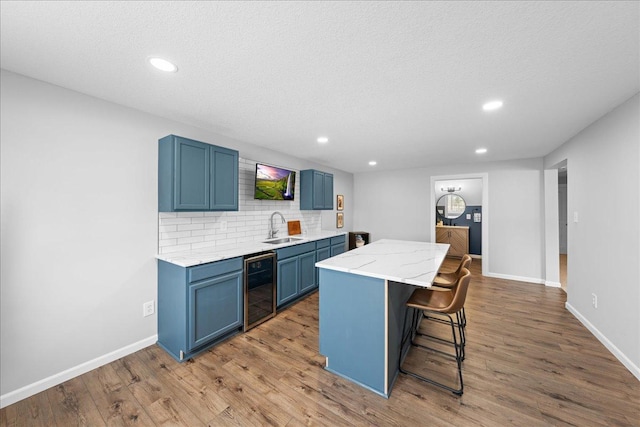 kitchen with wood finished floors, blue cabinetry, a sink, a center island, and wine cooler
