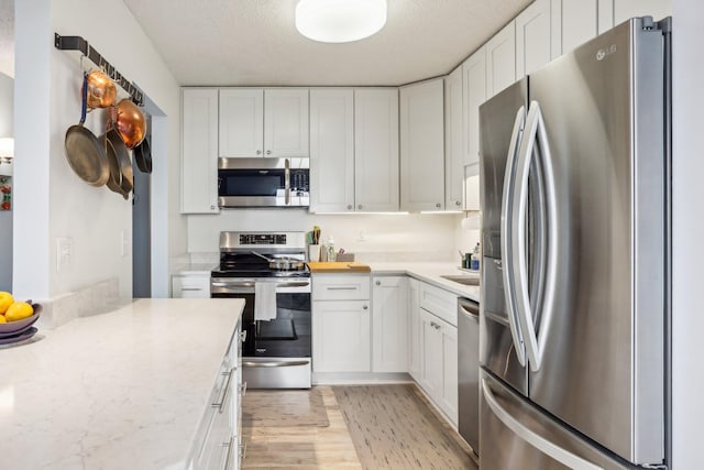 kitchen with a textured ceiling, white cabinets, stainless steel appliances, and light wood-style flooring
