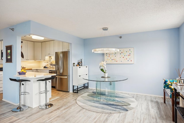 kitchen with appliances with stainless steel finishes, light countertops, baseboards, a peninsula, and light wood finished floors