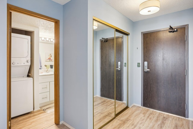 corridor featuring stacked washing maching and dryer, baseboards, light wood-type flooring, and a textured ceiling