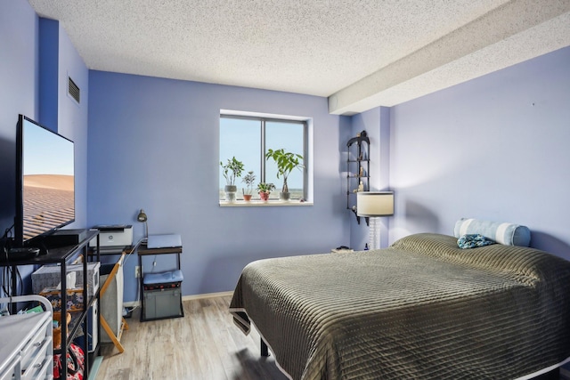 bedroom featuring baseboards, a textured ceiling, and wood finished floors
