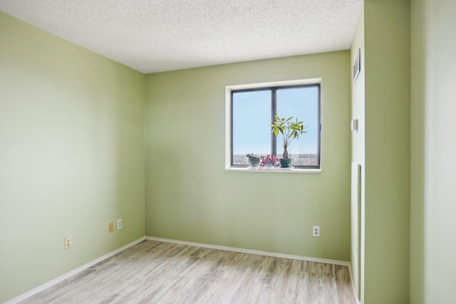empty room with a textured ceiling, baseboards, wood finished floors, and visible vents