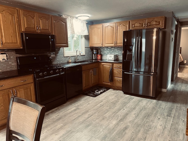 kitchen with black appliances, dark countertops, backsplash, light wood finished floors, and a sink