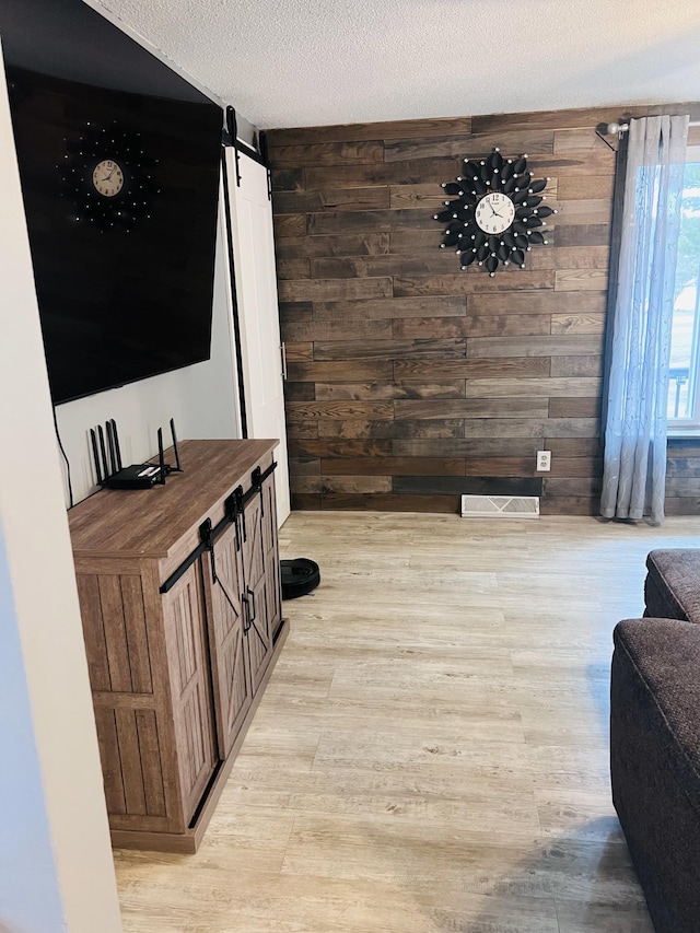 living area featuring visible vents, a barn door, light wood-style floors, and wood walls