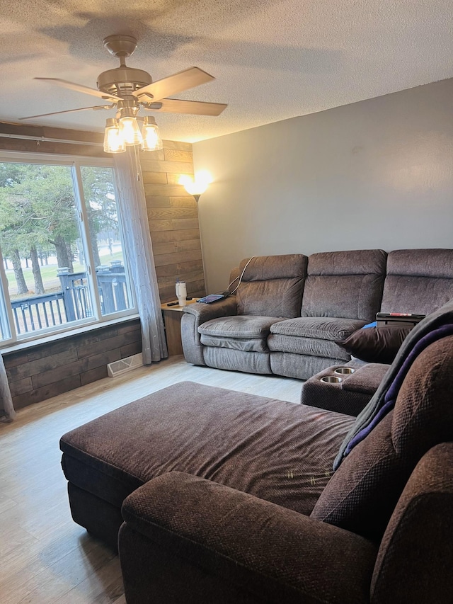 living area featuring a textured ceiling, ceiling fan, wood walls, and wood finished floors