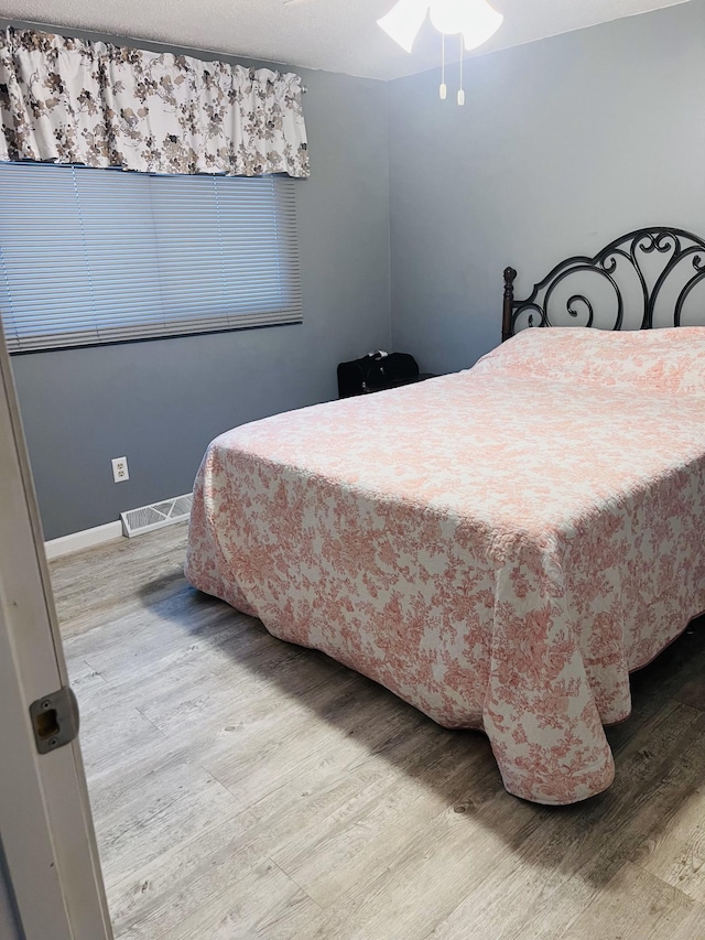 bedroom with baseboards, visible vents, and wood finished floors