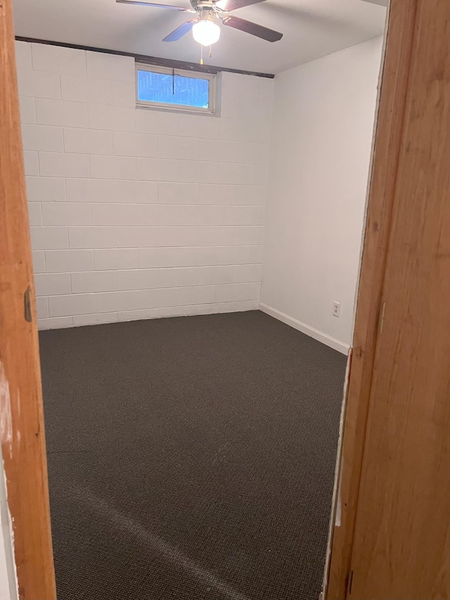 below grade area with concrete block wall, ceiling fan, and carpet floors