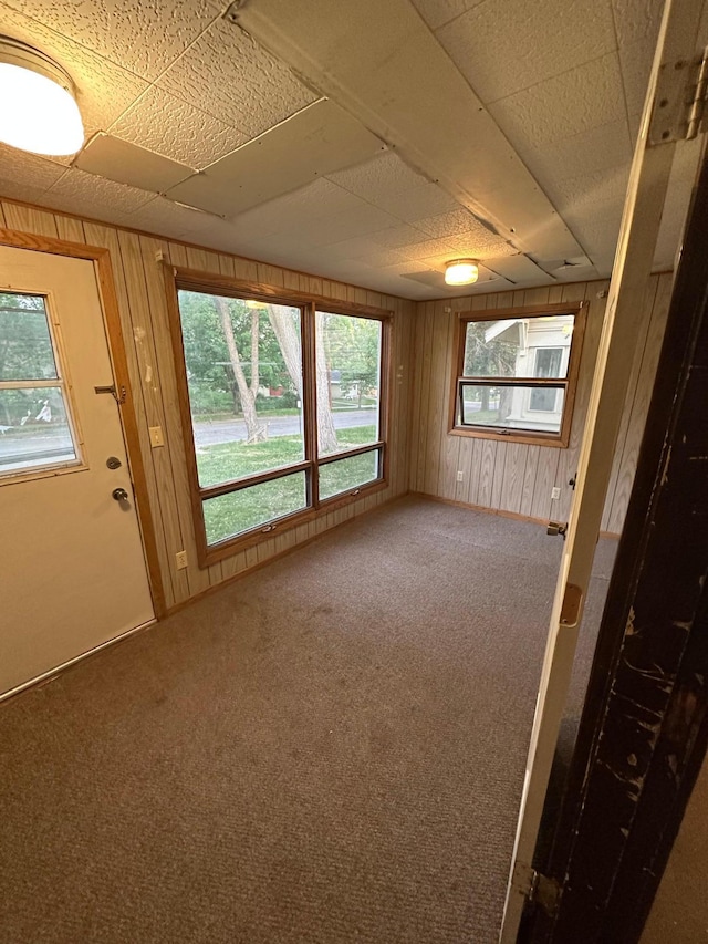 carpeted spare room featuring a drop ceiling and wooden walls