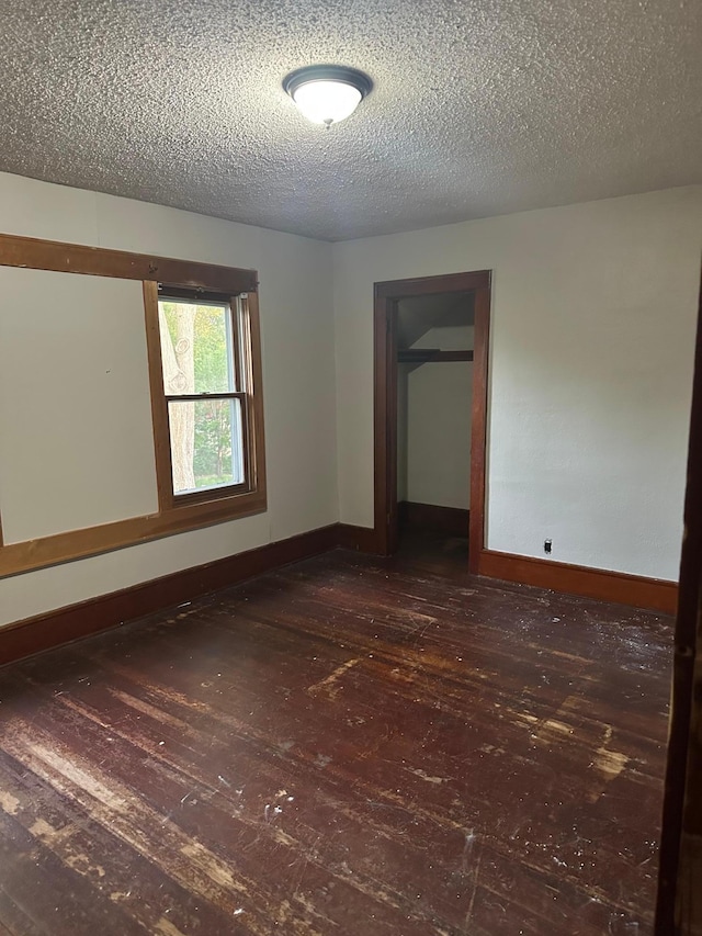 empty room featuring dark wood-style flooring, a textured ceiling, and baseboards