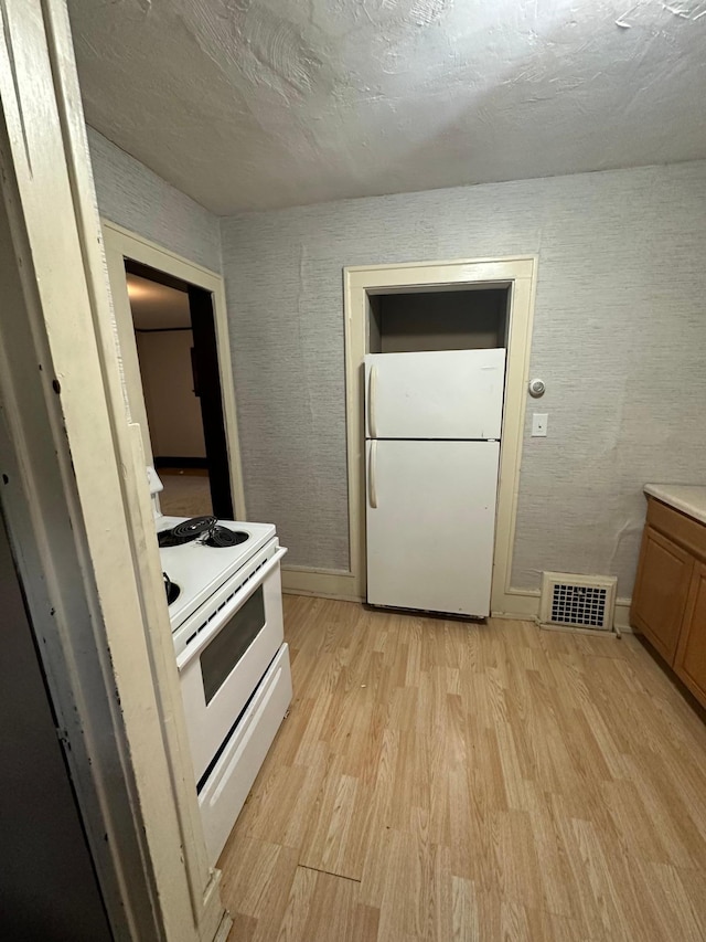kitchen featuring light wood-style flooring, visible vents, baseboards, white appliances, and light countertops