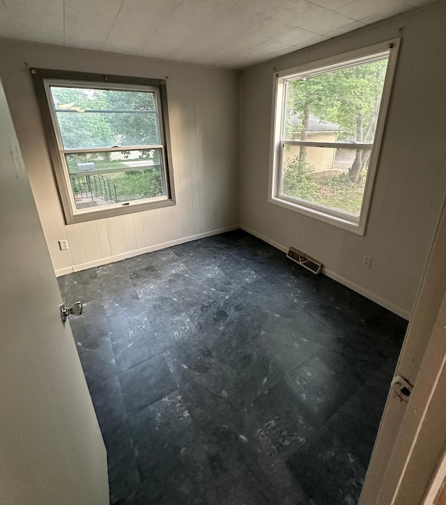 empty room featuring wood walls, visible vents, and baseboards