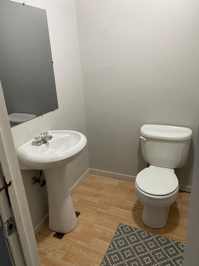 half bathroom featuring toilet, wood finished floors, and baseboards