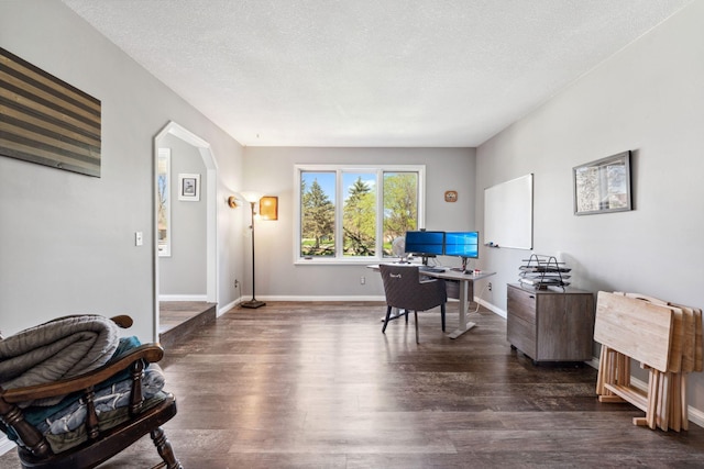 office area with arched walkways, a textured ceiling, dark wood finished floors, and baseboards