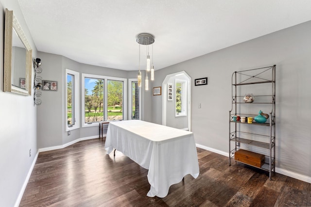 dining space featuring arched walkways, baseboards, and dark wood finished floors