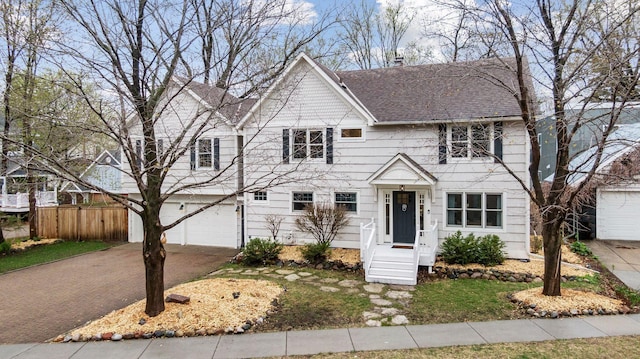 colonial home featuring roof with shingles, an attached garage, and driveway