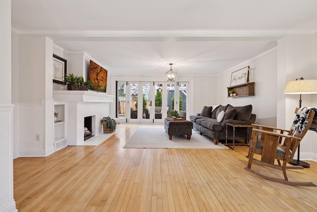 living room featuring wood-type flooring, a fireplace with flush hearth, crown molding, and visible vents