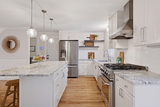 kitchen featuring open shelves, a sink, wall chimney exhaust hood, stainless steel appliances, and light wood-type flooring