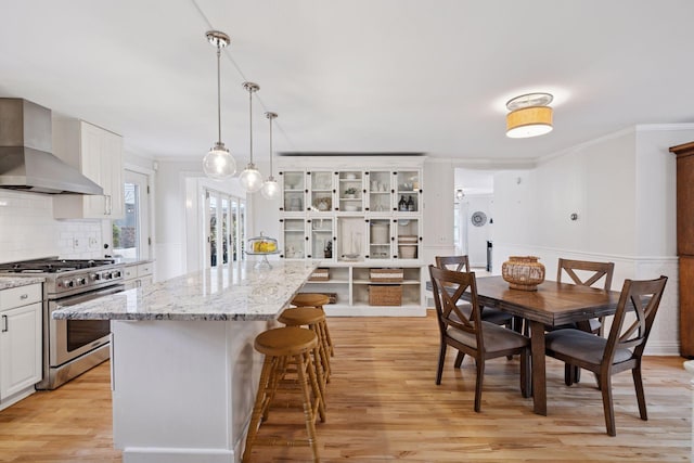 kitchen with wall chimney range hood, crown molding, gas stove, light wood finished floors, and a kitchen island