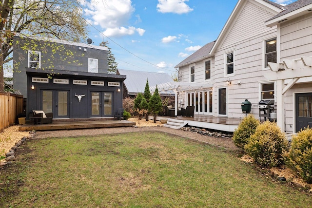 rear view of property featuring fence, a wooden deck, french doors, an outdoor structure, and a lawn