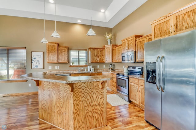 kitchen featuring a high ceiling, appliances with stainless steel finishes, a breakfast bar, and light wood-style flooring