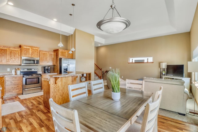 dining room with recessed lighting, a raised ceiling, light wood-type flooring, and stairs