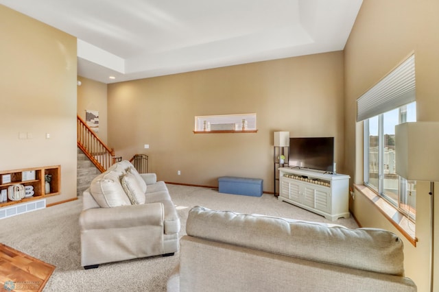 carpeted living area featuring baseboards, a tray ceiling, stairs, and visible vents