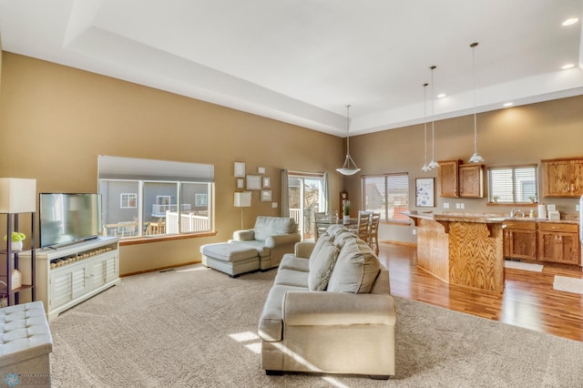 living area featuring recessed lighting, light carpet, a raised ceiling, and a towering ceiling