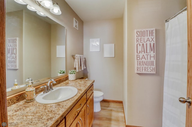 bathroom featuring vanity, toilet, baseboards, wood finished floors, and visible vents