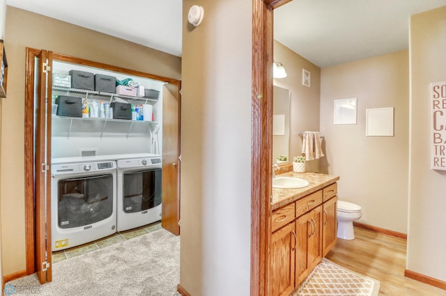 laundry area with laundry area, baseboards, light wood-type flooring, washing machine and clothes dryer, and a sink
