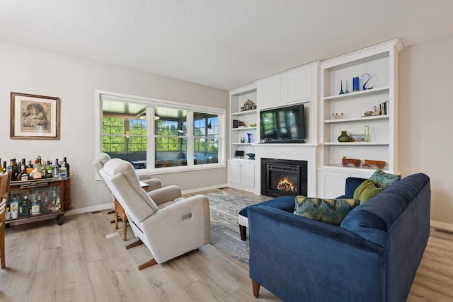 1703 11th St NE, Buffalo, MN 55313 - living room with light wood-style flooring, a glass covered fireplace, a textured ceiling, and baseboards