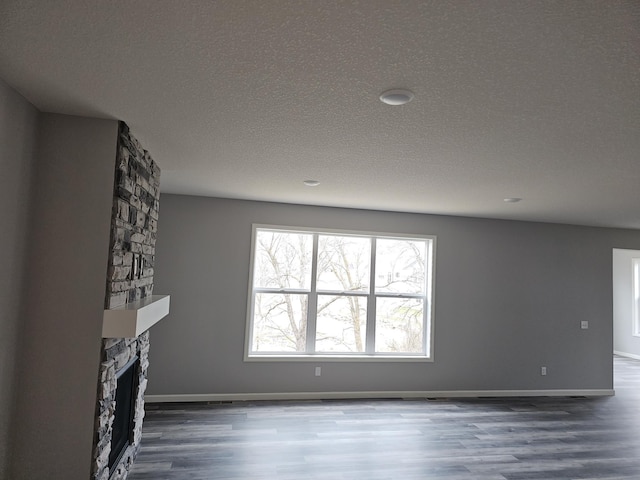 17121 61st St NE, Otsego, MN 55330 - unfurnished living room featuring a stone fireplace, baseboards, a textured ceiling, and wood finished floors