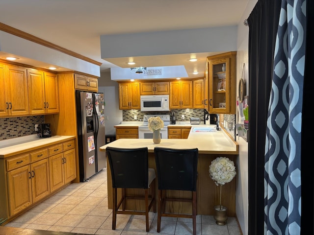 kitchen with decorative backsplash, a peninsula, brown cabinets, and white appliances
