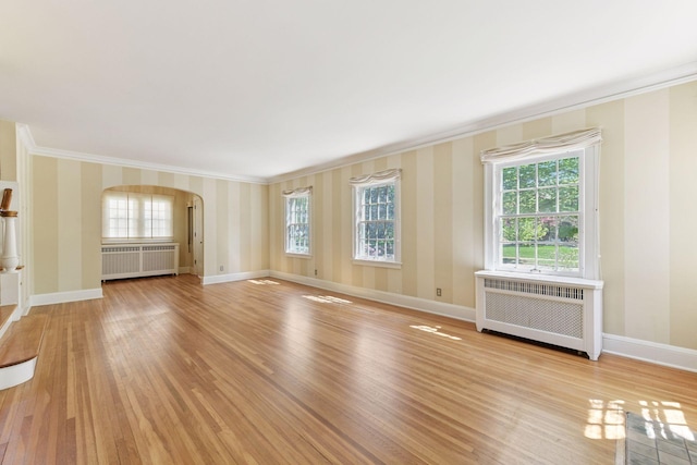4606 Drexel Ave, Edina, MN 55424 - unfurnished living room featuring radiator heating unit, ornamental molding, arched walkways, light wood-style floors, and plenty of natural light