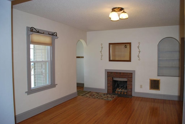 767 Shoreacres Dr, Fairmont, MN 56031 - unfurnished living room featuring a brick fireplace, visible vents, baseboards, arched walkways, and wood finished floors
