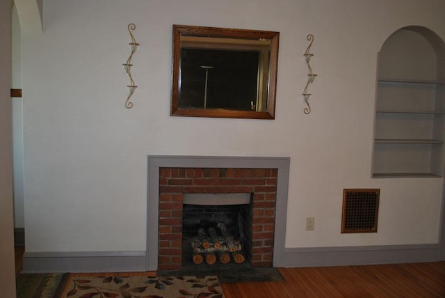 767 Shoreacres Dr, Fairmont, MN 56031 - living room featuring visible vents, arched walkways, a brick fireplace, wood finished floors, and built in shelves