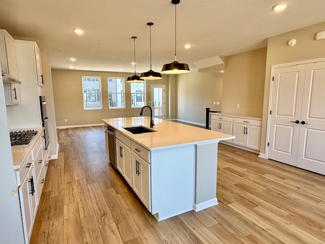 kitchen with light wood-type flooring, light countertops, white cabinets, and a sink