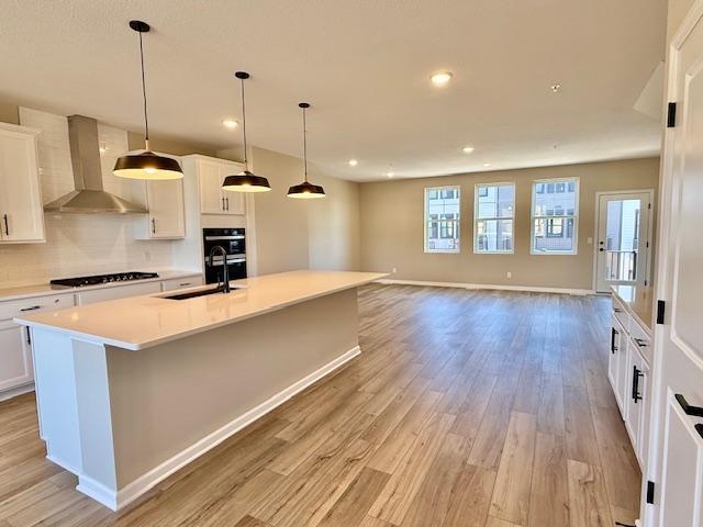 kitchen featuring a sink, light wood-style floors, black stovetop, and wall chimney exhaust hood