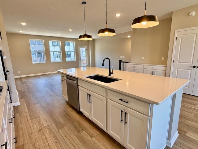 kitchen with a sink, light wood-type flooring, light countertops, stainless steel dishwasher, and open floor plan