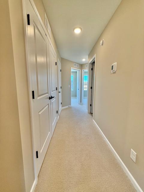 hallway featuring visible vents, light carpet, and baseboards